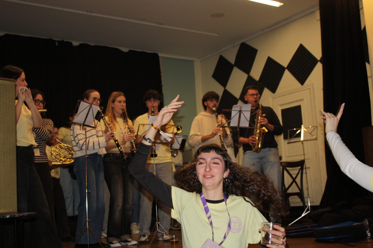 Estudiants de la UV amb instruments sobre l'escenari mentre una de les organitzadores salta, visiblement animada.